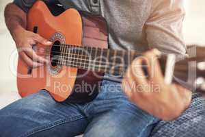 He lets the music flow from his hands. Shot of an unrecognizable man practising guitar at home.