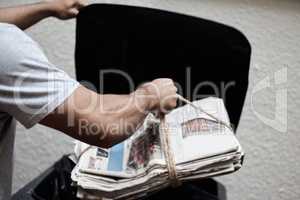 Doing my part to save the environment. Shot of a young man putting newspaper in the bin to be recycled.