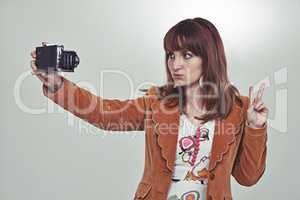 The seventies selfie. Cropped studio shot of a young woman in a vintage outfit taking a selfie with an old-fashioned camera.