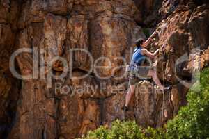 Hanging on tightly. A wide shot of a young woman rock climbing.