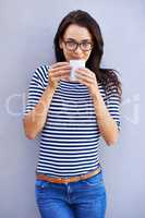 Now that's a fine brew. Portrait of a an attractive woman holding a coffee cup against a gray background.