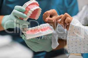 Learning how to floss. Shot of a unrecognizable dentist holding a pair of artificial gums and teeth while a young little patient flosses it.