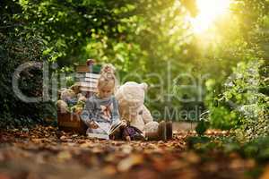 Nurture their curiosity. Shot of a little girl reading to her toys while out in the woods.