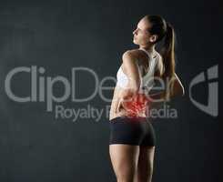 Thats painful. Studio shot of a sporty young woman holding her lower back in pain against a dark background.