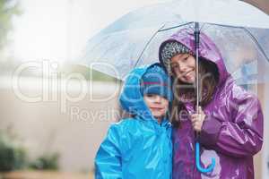 The rain never stopped us from having fun. Portrait of two siblings standing under an umbrella outside.