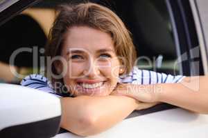 No distance is too far to find your happy place. Portrait of a young woman looking out of a car window during a road trip.