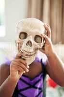 Taking my face off. Shot of an unrecognizable little child covering their face with a skull.