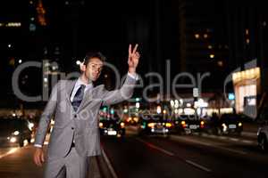 Taxi. A handsome businessman hailing a cab while standing in a busy city street at night.