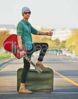 Taking his music on the road. Shot of a handsome young man hitchhiking at the side of the road with a guitar and suitcase.