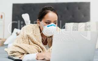 Keeping up with all the latest health advice. Shot of a woman wearing a mask while lying on her bed with her laptop.