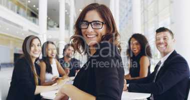 We're inviting you to the table. Cropped shot of a young businesswoman smiling in an office during a meeting with her colleagues in the background.