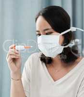 I check my temperature before I decide to head out. Shot of a woman wearing a mask while checking her temperature at home.