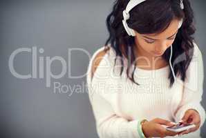 She never misses an episode of her favorite podcast. Studio shot of a young woman listening to music while using her phone against a gray background.