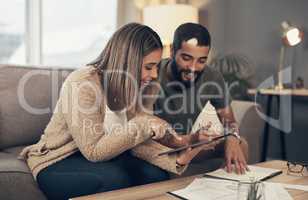 Improving their finances one tap at a time. Shot of a young couple sing a digital tablet while going through paperwork at home.