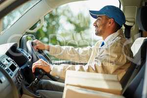 Hes a cardboard box chauffeur. Shot of a happy delivery man driving his van with boxes in the front seat.