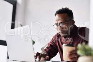 Surviving on coffee to get me through my work. Cropped shot of a handsome young businessman sitting alone and working on his laptop in the office.