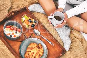 All neat and ready to eat. Aerial shot of an unrecognizable woman holding a cup of coffee while sitting with an arranged breakfast tray in bed.