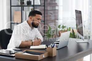 Sitting down for some thorough planning. Shot of a young businessman writing notes while working on a laptop in an office.