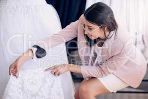 Because to brides, every detail matters. Shot of an attractive young seamstress working in a bridal boutique.