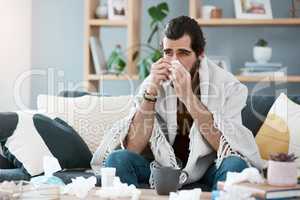 This is not how I planned on spending my weekend. Shot of a sickly young man blowing his nose with a tissue in his living room.
