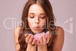 Making a wish. Gorgeous young woman blowing away a handful of rose petals on a pink background.