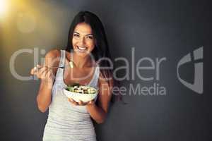 Healthy and delicious. Portrait of a healthy young woman eating a salad against a gray background.