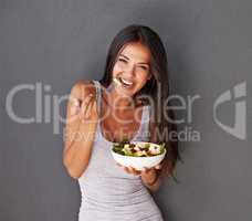 Salads - good for me. Portrait of a healthy young woman eating a salad against a gray background.