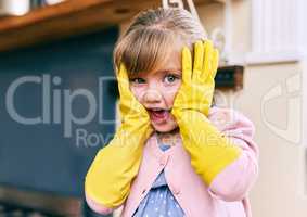 Oh no time to wash the dishes. Portrait of a surprised looking little girl holding her face wit her hands while wearing yellow dishwashing gloves.