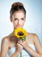 She makes flowers seem ordinary. Studio portrait of a beautiful young woman holding a sunflower.