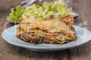 Lasagne mit Salat auf dunklem Holz