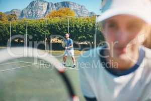 Challenge yourself everyday. Shot of a handsome young male tennis player outdoors on the court with a female teammate in the foreground.