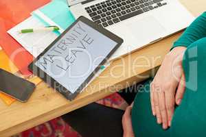 Not long now.... A pregnant woman sitting with a tablet with the words maternity leave on the screen.