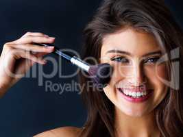 Highlighting her best features. Portrait of a gorgeous young woman with a makeup brush against a dark background.