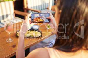 Those greasy cheat days. Rearview shot of an unrecognizable woman talking a picture of her meal at a restaurant outside.