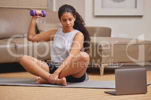Heres to stronger arms. Full length shot of a young woman using her laptop to follow an online fitness class in her living room.