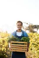 Know where your food come from. Shot of a young man holding a crate full of freshly picked produce on a farm.