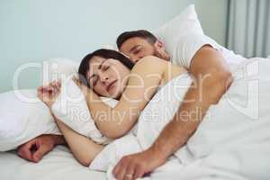 Too comfortable to get out of bed. Shot of a relaxed young couple sleeping in each others arms in bed during morning hours.