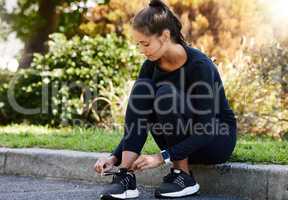 Making sure her laces are nice and tight. Full length shot of an attractive and athletic young woman tying her shoelaces while sitting on the curb outdoors.