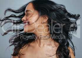 Her hair has natural bounce and great volume. Studio shot of an attractive young woman tossing her hair against a grey background.