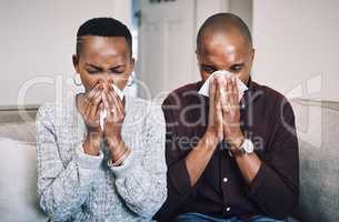 Were as sick as puppies today. Shot of a sickly young couple blowing their noses with tissues at home.