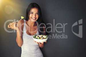 Grab a fork. Portrait of a healthy young woman eating a salad against a gray background.