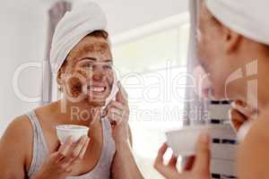 I cant wait to see the beautiful results after this. Cropped shot of an attractive young woman applying a coffee mask on her face while standing in front of the mirror in her bathroom at home.