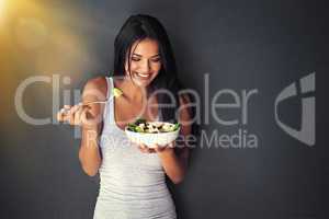 This is delicious. Shot of a healthy young woman eating a salad against a gray background.