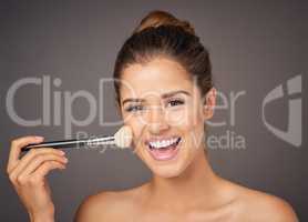 Rosy cheeks, here I come. Portrait of a beautiful young model applying blusher to her cheeks in studio.