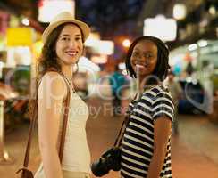 This city comes alive at night. Portrait of two happy young friends exploring a foreign city at night.