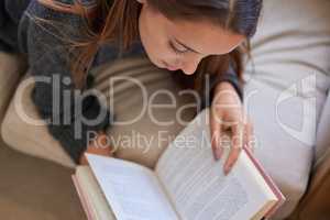 You enter another world once you open a book. High angle shot of a young woman reading a book at home.