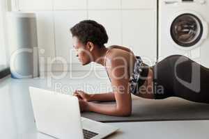 A plank hold engages multiple muscles at once. Shot of a young woman using a laptop while exercising at home.