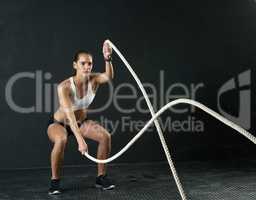These ropes really are a battle. Studio shot of an attractive young woman working out with heavy ropes against a dark background.