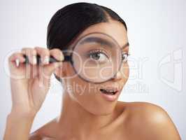 I see a new skincare trend up ahead. Studio shot of an attractive young woman looking through a magnifying glass against a grey background.