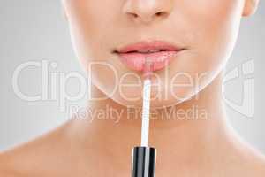 Beauty is in the skin. Shot of a unrecognizable young woman applying lipgloss to her lips against a grey background.